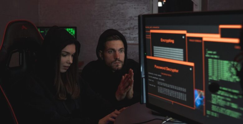 CAASM EASM CTEM what the acronyms mean for a security team 1 Cybersecurity experts in hoodies analyzing encrypted data on computer screens in an indoor setting.